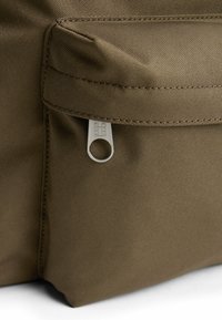 Bolsa de tela marrón con un bolsillo con cremallera y un tirador plateado. El material tiene una apariencia texturada y duradera.