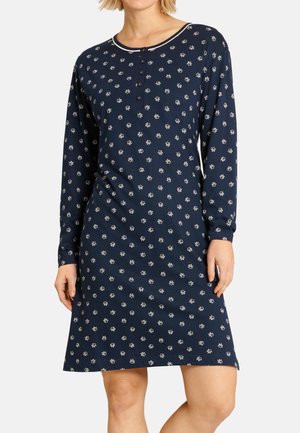 Frau trägt ein marineblaues langärmliges Kleid mit kleinen weißen Blumenmustern und einem geknöpften Ausschnitt.