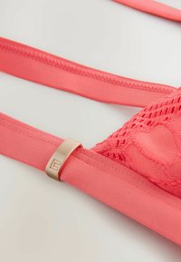 Koraal lingerie met doorschijnende kantdetails en soepele verstelbare bandjes. Voorzien van een metalen sluiting met een minimalistisch ontwerp.