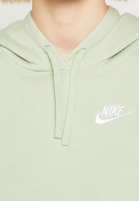 Ljusgrön huva med framficka, snoddar och en liten vit Nike-logotyp broderad på bröstet. Mjuk textur.