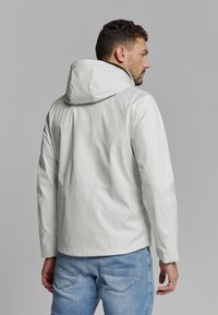 Lichtgrijze leren jack met een capuchon, met een rechte snit en subtiele stikdetails. Draagt met blauwe jeans, gezien van achter.