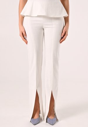 Pantaloni bianchi su misura con spacchi laterali, realizzati in tessuto leggero. Presentano una vestibilità dritta e una consistenza morbida. Abbinati a tacchi a righe blu navy.