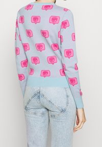 Ljusblå tröja med rosa grafiska mönster av pratbubblor med ögon. Ribbade manschetter och nederkant med en slät textur, figursydd design.