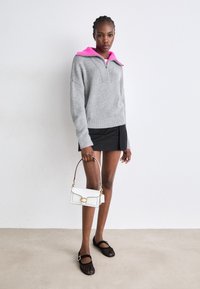 Grijze gebreide pullover met roze kraag, zwarte rok, zwarte platte schoenen en witte handtas met gouden accenten. Eenvoudig ontwerp, casual stijl.