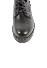 Scarpa in pelle nera con punta arrotondata, perforazioni decorative e design con lacci. Suola in gomma notevole con borchie metalliche lungo il bordo.
