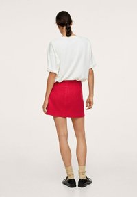 Camiseta blanca de gran tamaño combinada con una minifalda de punto texturizado en rojo brillante. Medias de color neutro y zapatos negros completan el look.