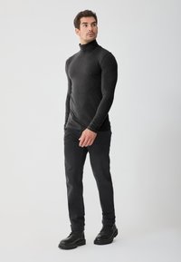 Pulover negru cu guler înalt, cu mâneci lungi, design ajustat, asortat cu blugi gri închis și cizme negre cu șireturi. Fundal simplu.