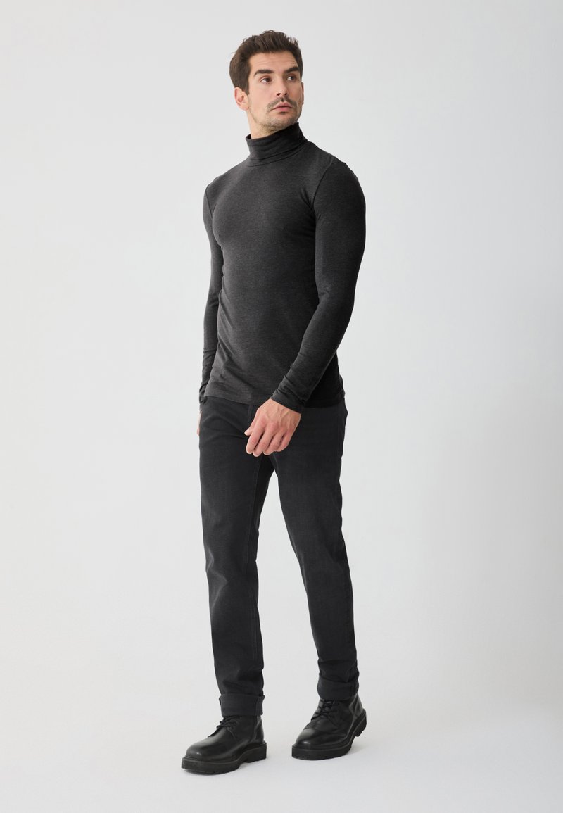Pulover negru cu guler înalt, cu mâneci lungi, design ajustat, asortat cu blugi gri închis și cizme negre cu șireturi. Fundal simplu.