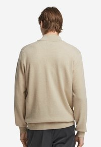 Beige stickad pullover med krage, featuring ribbade manschetter och nederkant. Mjuk textur, avslappnad passform och minimalistisk design på baksidan.