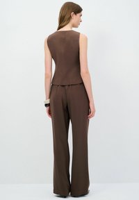 Top sin mangas marrón con un corsé ajustado y pantalones anchos a juego, que presentan una textura suave y un diseño minimalista.