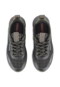 Para czarnych i oliwkowych sneakersów HUGO z kształtowanymi językami z wzorzystymi pętelkami oraz markowymi wkładkami, widziana z góry na białym tle.