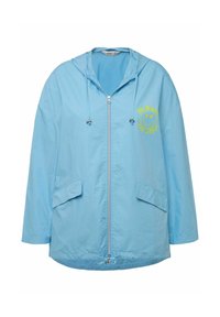 Chaqueta cortavientos azul claro con capucha, cremallera frontal y dos bolsillos laterales. Presenta el texto amarillo "HACE LO QUE AMAS" y una cara sonriente.