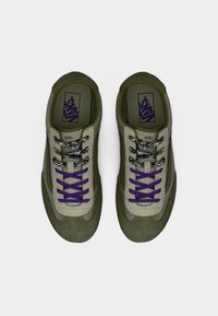 Paire de baskets Vans vert olive avec tige en matériaux mixtes, lacets noirs et blancs à motifs, et lacets plats violets sur une languette beige.