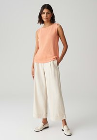 Pull sans manches orange clair avec une texture douce, associé à un large pantalon crème et des mocassins blancs. Design simple et décontracté.