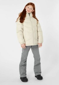 Puffige cremefarbene Jacke mit zipfremem hoher Kragen, kombiniert mit grauen Hosen und schwarzen Stiefeln. Die Jacke weist horizontale Steppabschnitte auf.