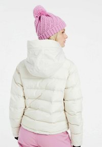 Witte pufferjack met een capuchon, voorzien van gestikte delen en een gladde textuur. Gecombineerd met een gebreide roze beanie met een pompon.