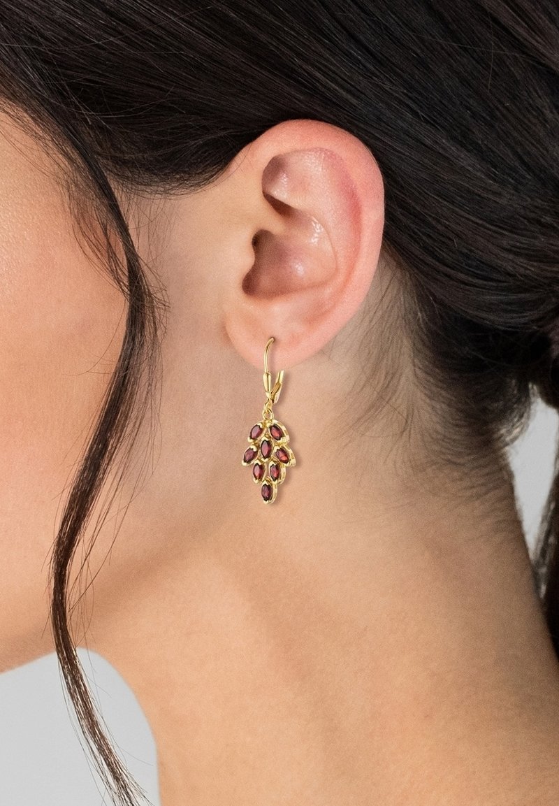 Boucles d'oreilles dorées présentant un design en forme de feuille avec plusieurs petites pierres précieuses rouges. Les boucles d'oreilles sont suspendues à un fermoir en anneau.