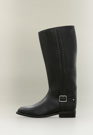 Botte d'équitation haute en cuir noir avec boucle latérale et couture décorative le long de la tige supérieure.