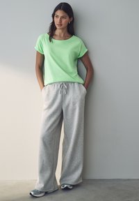 T-shirt verde chiaro a maniche corte con risvolti abbinato a pantaloni da tuta grigi a gamba larga. Tessuto testurizzato, vestibilità casual e vita con cordino.