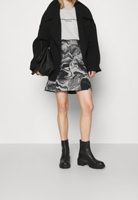 Černý oversized kabát, šedé grafické tričko, vzorovaná mini sukně s černým a šedým mramorovým designem a černé robustní kotníkové boty.