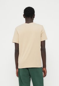 Μπεζ κοντομάνικη μπλούζα από βαμβάκι με στρογγυλή λαιμόκοψη. Η πλάτη είναι απλή, με άνετη εφαρμογή και ίσια γραμμή στο τελείωμα.