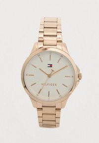 Námořnické hodinky z růžového zlata s propojeným p�áskem, béžovým ciferníkem, minimalistickými hodinovými značkami a logem Tommy Hilfiger na pozici 12 hodin.