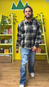 Plaid shirt in black and white, long sleeves, relaxed fit; light blue jeans, white sneakers; bright yellow background with green shelves.