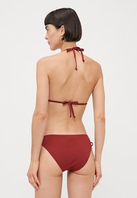Crimson two-piece bikini, featuring a halter neck with tie closure and a minimalist design. Smooth fabric with a matte finish.