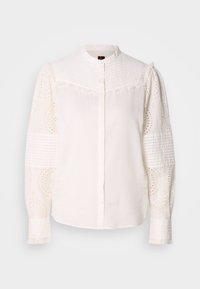Camicia bianca con colletto alto, parte superiore tessurizzata e maniche in pizzo ad occhielli ricamate con motivi intricati e dettagli arricciati.