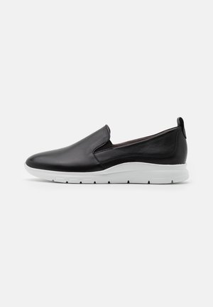 Zapatos negros sin cordones hechos de cuero liso, con una suela blanca de goma y un diseño minimalista sin elementos visibles.