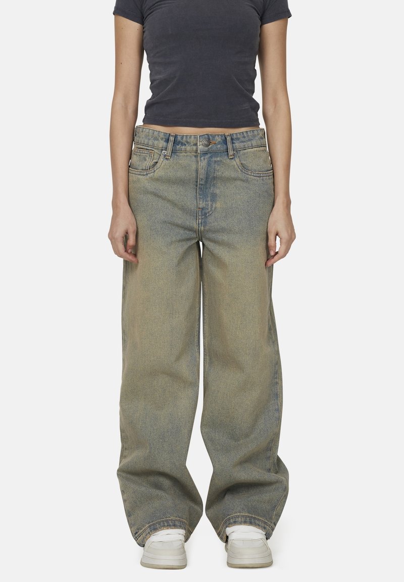 Jasnoniebieskie dżinsowe spodnie o szerokich nogawkach z wyblakłym wzorem, z pięcioma kieszeniami, zapięciem na guzik i przeszyciami. Noszone z białymi trampkami.