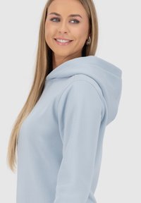 Felpa blu chiaro con una texture morbida e un grande cappuccio. Presenta maniche lunghe e una vestibilità rilassata, mettendo in mostra un design semplice e moderno.