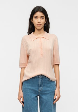 Jasnoróżowa prążkowana koszulka polo z krótkim rękawem, z zapięciem na guziki z przodu i klasycznym kołnierzykiem, w połączeniu z niebieskimi jeansami z wysokim stanem.