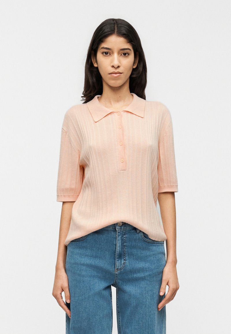 Ανοιχτό ροζ ριμπ πλεκτό πόλο με κοντά μανίκια, με κουμπωτό μπροστινό μέρος και κλασικό γιακά, συνδυασμένο με μπλε τζιν ψηλόμεσο.