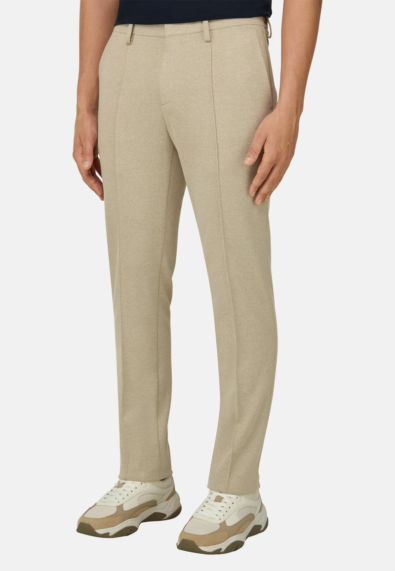 Pantalon beige ajusté avec coutures avant porté avec des baskets épaisses beige et blanches sur fond blanc.