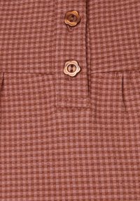 Braun karierter Stoff mit einer weichen Textur, verziert mit dekorativen, blumenförmigen Knöpfen in Kupfertönen und dezenten Falten am unteren Rand.