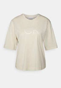Beige bomulds t-shirt med korte ærmer, rund hals og prægede "CK" logo foran. Blød tekstur og afslappet pasform.