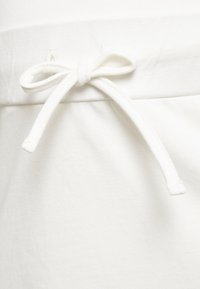 Tecido branco com uma textura suave, apresentando uma cinta de tecido na cintura. A cinta está amarrada em um laço, destacando um design casual.