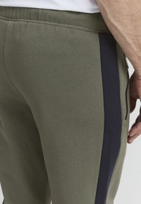 Olive green joggers with a textured finish, featuring a navy side stripe and zippered pocket detail, designed for comfort and functionality.
