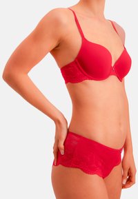 Roter BH mit glatten Cups und Spitzenakzenten; passende rote Spitzenshorts mit gewellten Kanten; beide verfügen über ein nahtloses Design.
