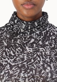 Langarm turtleneck top met een zwart-wit abstract patroon, zachte stof, slanke pasvorm en een hoge halslijn.