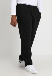 Black jogger pants with elastic waistband, side pockets, and cuffed hems, paired with white sneakers. Smooth fabric texture.