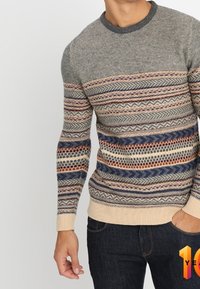 Stickad tröja i grått med flerfärgade horisontella mönster; rund halsringning; ribbade ärmslut och nederkant; tyget verkar mjukt och texturerat.