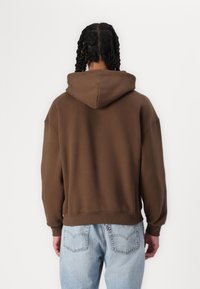 Sweatshirt capuz castanho com um corte descontraído, punhos canelados e uma bainha reta. Feito de tecido suave, apresenta um design simples sem padrões.