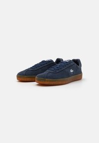 Zapatillas de ante azul marino con suela de goma, que cuentan con cordones planos y un pequeño logotipo en el lateral, diseñadas para un uso casual.