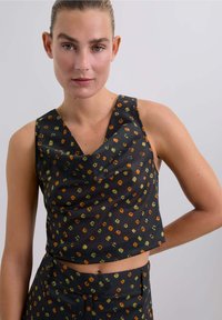 Top corto negro con escote tipo drapeado, que presenta un patrón de formas geométricas en naranja y verde. Tejido suave con una textura blanda.