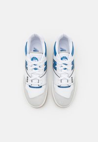 Chaussures de sport blanches avec des accents bleus, combinant cuir et daim, design à lacets, et semelle en caoutchouc. Numéro de modèle 550 visible.