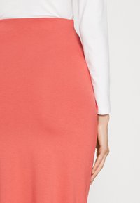 Koralli midi-hame, jossa on sileä tekstuuri ja kevyt venyvyys. Korkea vyötärösuunnittelu yhdistettynä muotoilultaan tiiviseen valkoiseen pitkähihaiseen puseroon.