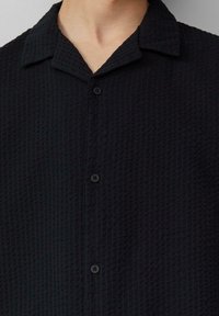 Zwart gestructureerd shirt met korte mouwen en een kraaghals, voorzien van vijf knopen aan de voorkant en een subtiel ruitpatroon.