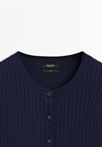 Navy blue knitted cotton cardigan with round neckline and black buttons, showing the upper section including the label.